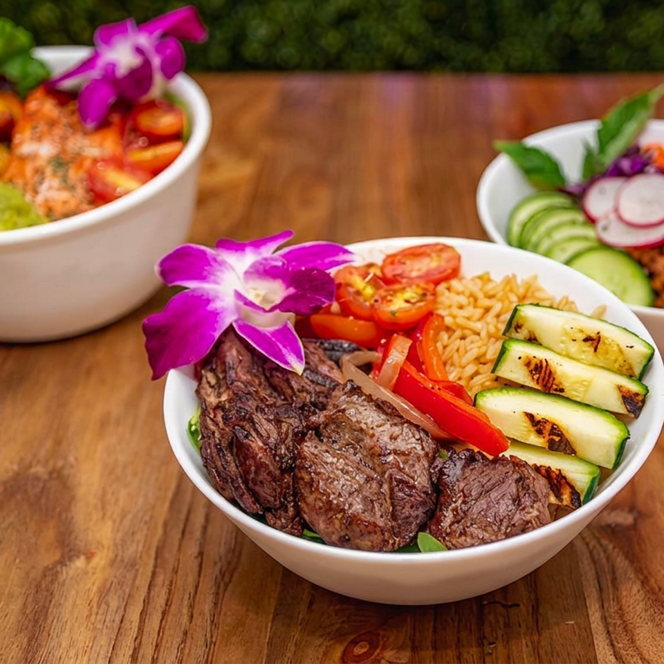 Three colorful rice bowls with grilled steak, vegetables, guacamole, and edible purple flowers on a wooden table.